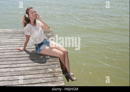 Frau, Musikhören und sitzen auf der Promenade am See, Ammersee, Oberbayern, Deutschland Stockfoto