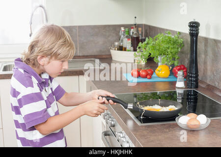 Junge Vorbereitung Spiegeleier in Küche, Bayern, Deutschland Stockfoto