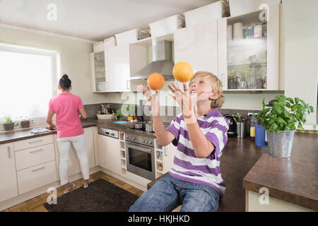 Junge Jonglieren mit Orangen während Mutter bereitet Essen, Bayern, Deutschland Stockfoto