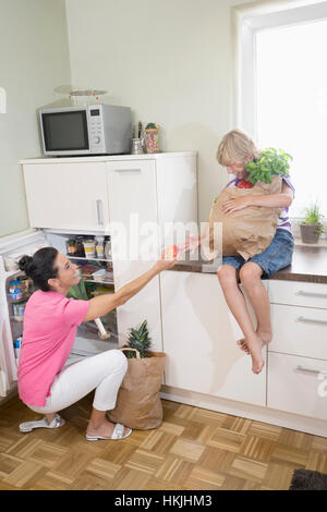 Frau geben einen Apfel zu ihrem Sohn am Kühlschrank, Bayern, Deutschland Stockfoto