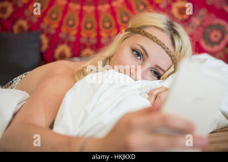 Schöne junge Frau mit Smartphone in das Schlafzimmer, Bayern, Deutschland Stockfoto