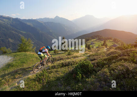 Mountainbiker fahren weiter bergan in alpiner Landschaft bei Sonnenuntergang, Zillertal, Tirol, Österreich Stockfoto