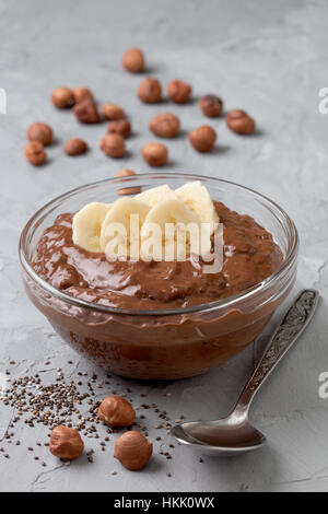 Schokolade Haselnuss Chia Pudding mit Banane in eine Glasschüssel auf grauem Beton Hintergrund Stockfoto