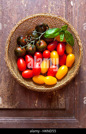 Multicolor rote und gelbe Kirschtomaten in einem hölzernen Korb mit frisch gepflückten frischen Basilikum Stockfoto