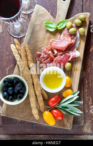 Wurst auf einem Holzbrett mit roten Tomaten, Oliven und andere Zutaten für einen Mittagssnack. auf einem alten Baum. und Rotwein Stockfoto