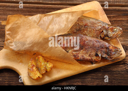 Gebackener Fisch mit Kartoffeln eingewickelt in Papier auf Holz Hintergrund Stockfoto