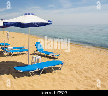 Sonnenschirme von weißen und blauen Farben und blauen Chaise Lounges am Sandstrand und Meer, aufgenommen am Sants Constantine und Helen Resort, Bulgarien. Stockfoto