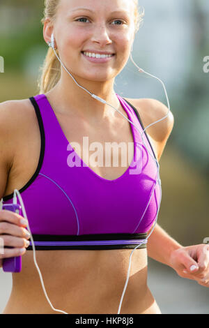 Close-up Schuss von jungen blonden Mädchen in ihren 20ern gerne joggen und tragen Kopfhörer Musik hören. Stockfoto