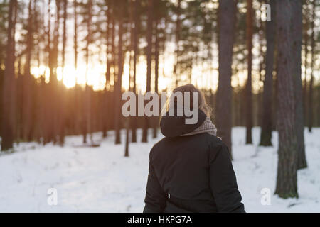 Teen Mädchen gehen im Winter Kiefernwald im Sonnenuntergang von hinten Stockfoto