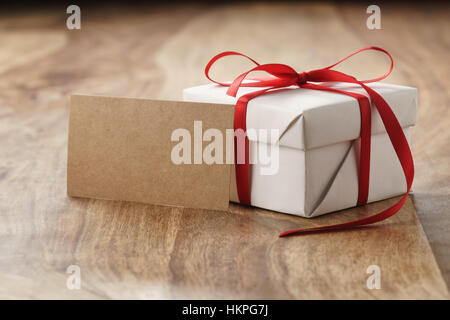 White-Paper Geschenkbox mit dünnen roten Band und Papierkarte auf alten Holztisch Stockfoto