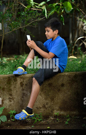 Kind mit Telefon sitzen in konkrete grünen Garten Stockfoto