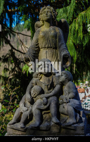 ein stehender Engelsstatue hinter sitzen Kinder im Garten mit Blatt Hintergrund Stockfoto