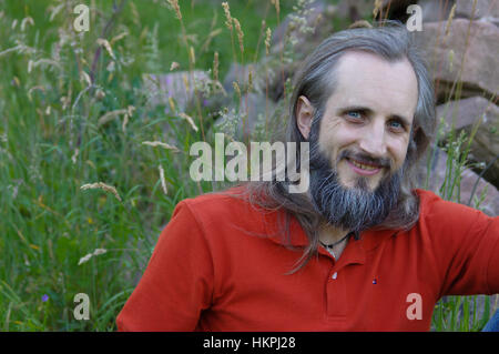 ein bärtiger glücklicher Mann sitzen in einem grünen Hintergrund an sonnigen Tag, Portrait Stockfoto