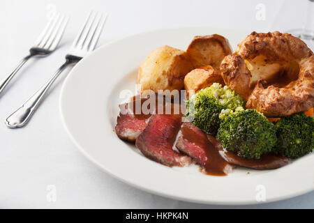 Traditionelle britische Braten Abendessen seltene Rindfleisch, Yorkshire Pudding, Bratkartoffeln und Brokkoli mit Sauce. Stockfoto