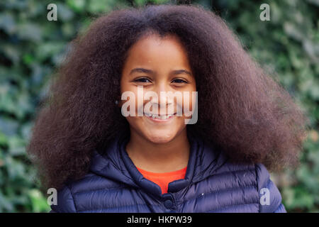 Hübsches Mädchen mit langen Afro-Haar im Garten mit einem blauen Mantel Stockfoto