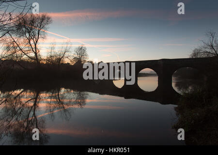 Dorf von Farndon, England. Malerischer Blick auf den Sonnenuntergang von der Klasse 1 aufgeführten 14. Jahrhundert mittelalterliche Holt Brücke über den Fluss Dee. Stockfoto