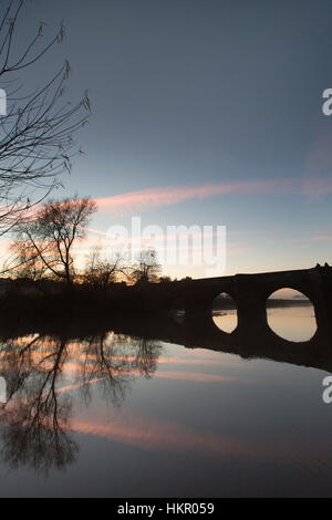 Dorf von Farndon, England. Malerischer Blick auf den Sonnenuntergang von der Klasse 1 aufgeführten 14. Jahrhundert mittelalterliche Holt Brücke über den Fluss Dee. Stockfoto