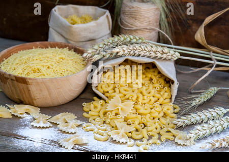 Italienische Teigwaren Farfalle, Ellenbogen Makkaroni und Fusilli in Leinwand wenig Tasche, verstreuten Mehl mit Ähren auf dunklem Holz Stockfoto