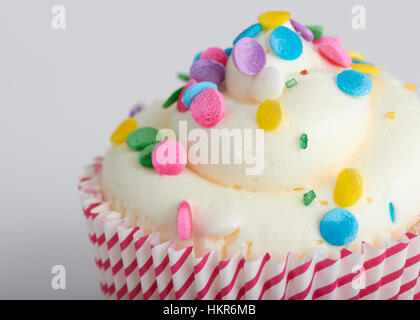 Eine Nahaufnahme Bild von einem Cupcake mit einem Wirbel von weißen Zuckerguss und bunten Streuseln obendrauf gemischt. Die Cupcake hat eine rote-weiße gestreifte Verpackung Stockfoto