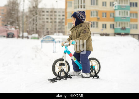 Junge auf Fahrrad mit Skiern wird vorbereitet von den Bergen im Schnee nach unten verschieben Stockfoto