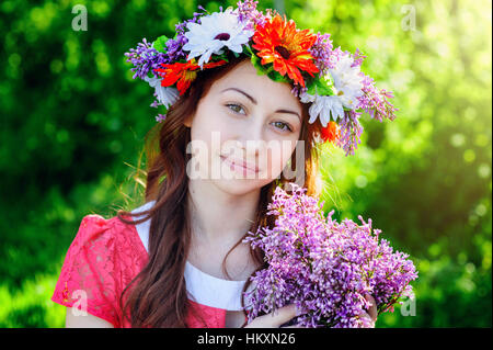 schöne junge Frau mit einem Kranz auf dem Kopf und den Duft von Flieder Stockfoto