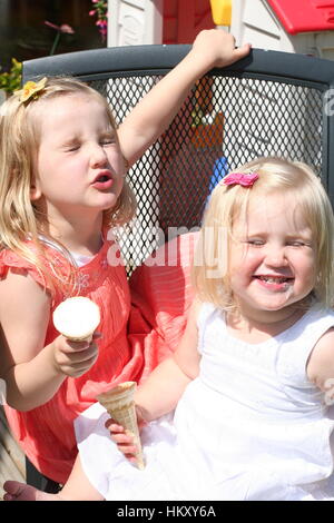 Zwei blonde Mädchen, Kinder Kinder lachen verwirren, die Gesichter essen Icecream cones Garten Best Life, schwindlig glücklich Konzept, Freude Glück spaß Sonne Stockfoto