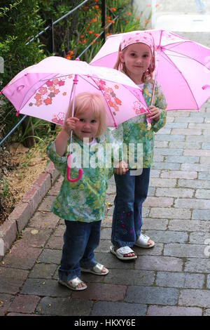 Gerne kleine blonde Mädchen, Kinder Kinder spielen offen pink Regenschirme tragen passende Regenjacken, Kleidung, Outfits Kindheit Konzept, rosa grün Stockfoto