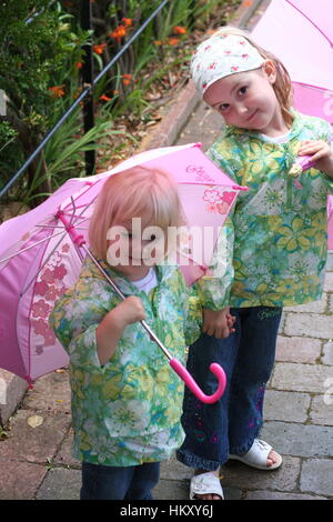 Glückliche kleine blonde Mädchen, Kinder Kinder spielen mit offenen rosa Regenschirme tragen passende Regenjacken, Kleidung, Outfits wetter Konzept, Sommer Regen Stockfoto