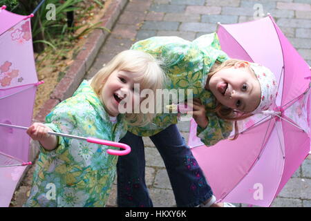 Kleine Mädchen, Kinder Kinder spielen offen pink Regenschirme tragen passende Regenjacken, Freude, happy, Spielen, verspielt, Geschwisterliebe, Wetter Stockfoto