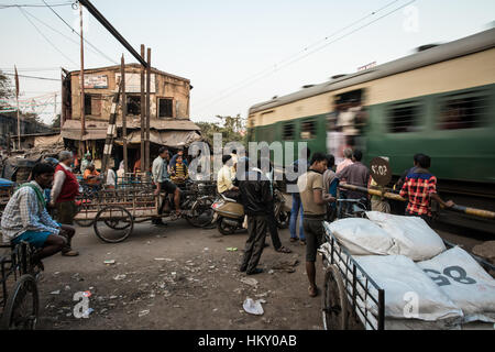 Ein Zug rast durch ein Bahnübergang als Zyklus Rikschas warten in der Nähe von Mallick Blumenmarkt in Kolkata (Kalkutta), Indien. Stockfoto