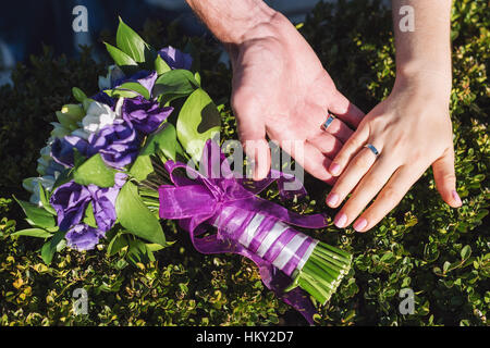 Brautpaar mit Trauringe Closeup. Paar legen ihre Hände auf Strauß Stockfoto