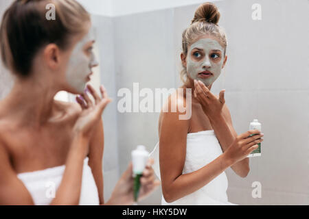 Junge Frau Auftragen der Maske Creme auf Gesicht im Badezimmer. Weibchen in Beauty-Behandlung auf ihre Gesichtshaut vor Spiegel nach Bad zu tun. Stockfoto