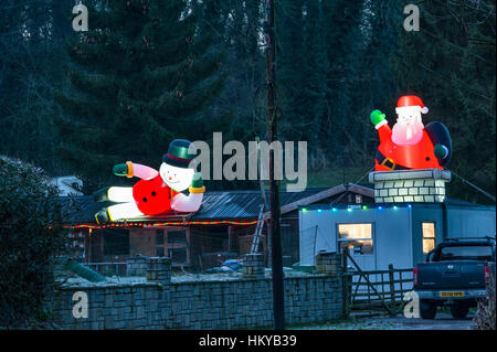 Riesige beleuchtete aufblasbare Weihnachtsfiguren umgeben eine abgelegene Hütte in der Nacht in ländlichen Herefordshire, England. Stockfoto