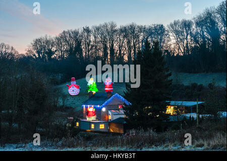 Riesige beleuchtete aufblasbare Weihnachtsfiguren umgeben eine abgelegene Hütte in der Nacht in ländlichen Herefordshire, England. Stockfoto