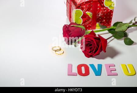 Valentines Tag rote Rosen mit Steinen verzierte Verlobungsringe und wickelte Geschenk. weißer Raum für Liebe Inhalt der Nachricht. Stockfoto