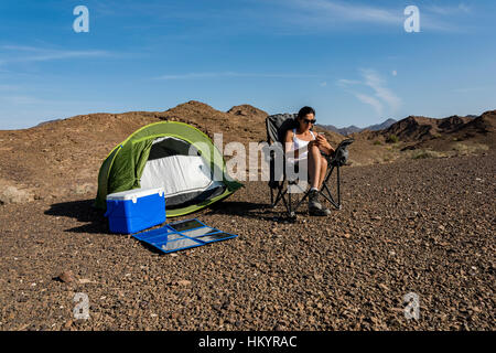 Frau in den Bergen mit ihrem Smartphone zu spielen, während des Ladevorgangs mit einem faltbaren Solarpanel. Stockfoto