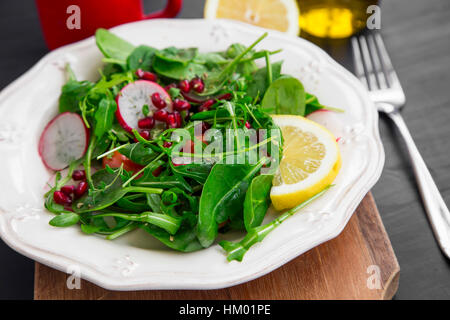 Gesunder Salat mit Baby-Spinat, Rucola, Radieschen und Granatapfel, gewürzt mit Zitrone Stockfoto