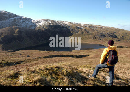 Hill-Walker stehen auf Hügel in der Ansicht unten zu bewundern, See Llyn Llygad Rheidol mit schneebedeckten Bergen im Hintergrund an sonnigen Tag Stockfoto