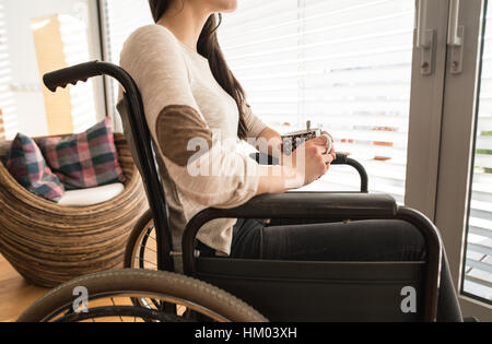 Nicht erkennbare junge behinderte Frau im Rollstuhl zu Hause. Stockfoto