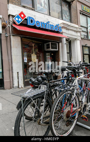 Ein Bündel von Fahrrädern sind verkettet zu einem Regal in der Nähe der Eingang zu Pizza Store ist eine lokale Domino. Stockfoto