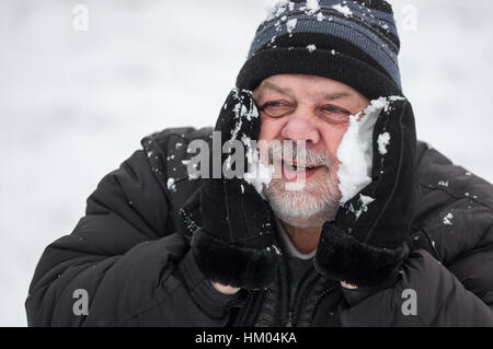 Porträt der ältere Mann seine Wangen reiben mit Schnee Aufwärmen Stockfoto