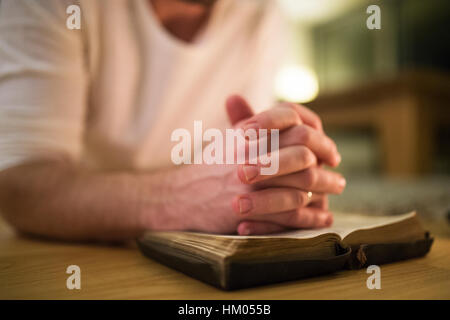 Nicht erkennbare Mann, der betet, kniend auf dem Boden, die Hände auf Bibl Stockfoto