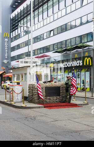 Ein Mann gekleidet wie eine Wache mit der amerikanischen Flagge am Checkpoint steht Charlie in Berlin Deutschland. Im Hintergrund kann ein McDonalds-Restaurant gesehen. Stockfoto