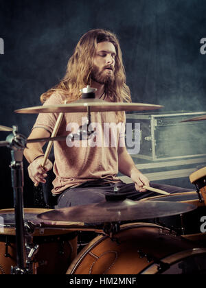 Foto von einem jungen männlichen Schlagzeuger mit langen Haaren sein Schlagzeug zu spielen. Gefiltert für Vintage-Look. Stockfoto