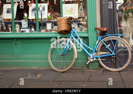 Alte blaue Damenrad mit einem Warenkorb auf der Vorderseite eines alten Schaufenster gelehnt wicker Stockfoto