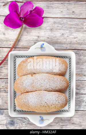 Overhead Schuss der Platte mit Savoiardi Biscuits (Löffelbiskuits) auf Holz Hintergrund mit Alpenveilchen Blume verziert. Stockfoto