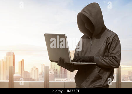 Hacker-Mann mit anonymen Maske mit Laptop zu hacken in das moderne Gebäude Stockfoto