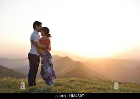 Paar in Liebe treffen Sonnenuntergang in grüne Hügel-Landschaft Stockfoto