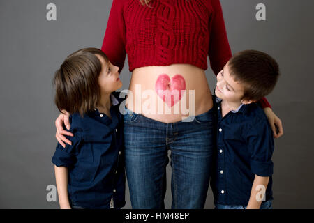 Schöne Kinder im Vorschulalter, Brüder, umarmt ihre schwangere Mutter, freudig erwartet großen Brüder zu sein. Rote Heide auf Mütter Bauch gezogen, küssen Stockfoto