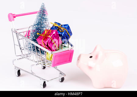 Warenkorb mit Weihnachtsbaum, Geschenke und Schwein Spardose auf weiß Stockfoto